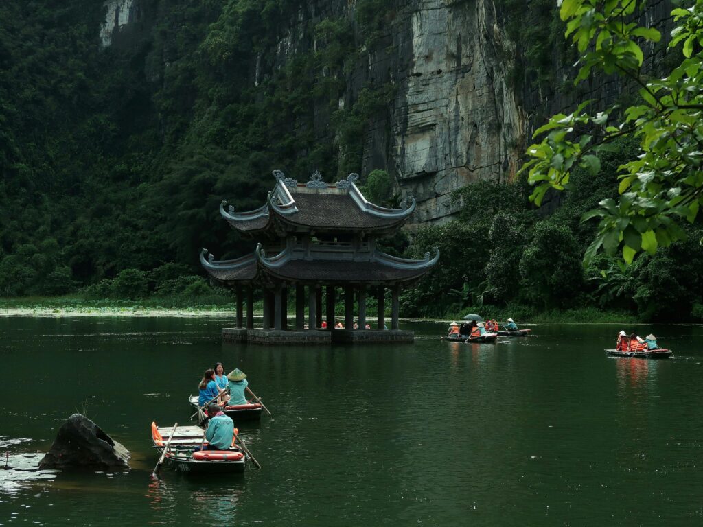 Traditional boats navigate the serene waters of Ninh Bình with lush karst landscape backdrop.